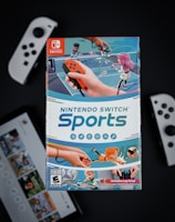 A box of Nintendo Switch Sports is prominently featured, surrounded by various Nintendo Switch controllers and a screen displaying a related interface. The box art depicts animated characters playing sports, such as tennis, with vibrant colors and action-oriented poses.