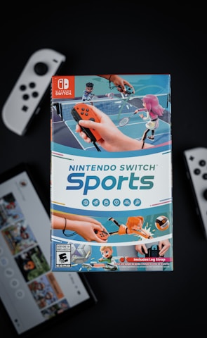 A box of Nintendo Switch Sports is prominently featured, surrounded by various Nintendo Switch controllers and a screen displaying a related interface. The box art depicts animated characters playing sports, such as tennis, with vibrant colors and action-oriented poses.